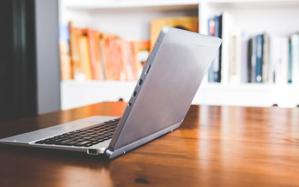 A laptop open on a wooden desk with bookshelves in the background, used as a student laptop buying guide cover.
